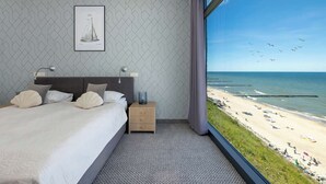 Ein Hotelzimmer mit Bett, Nachttischen, einem gerahmten Bild und Blick auf den Strand.