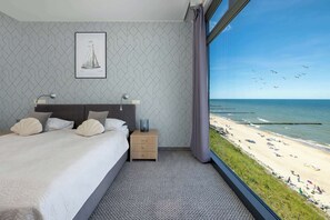 Una habitación de hotel con cama, mesitas de noche, un cuadro enmarcado y vistas a la playa.