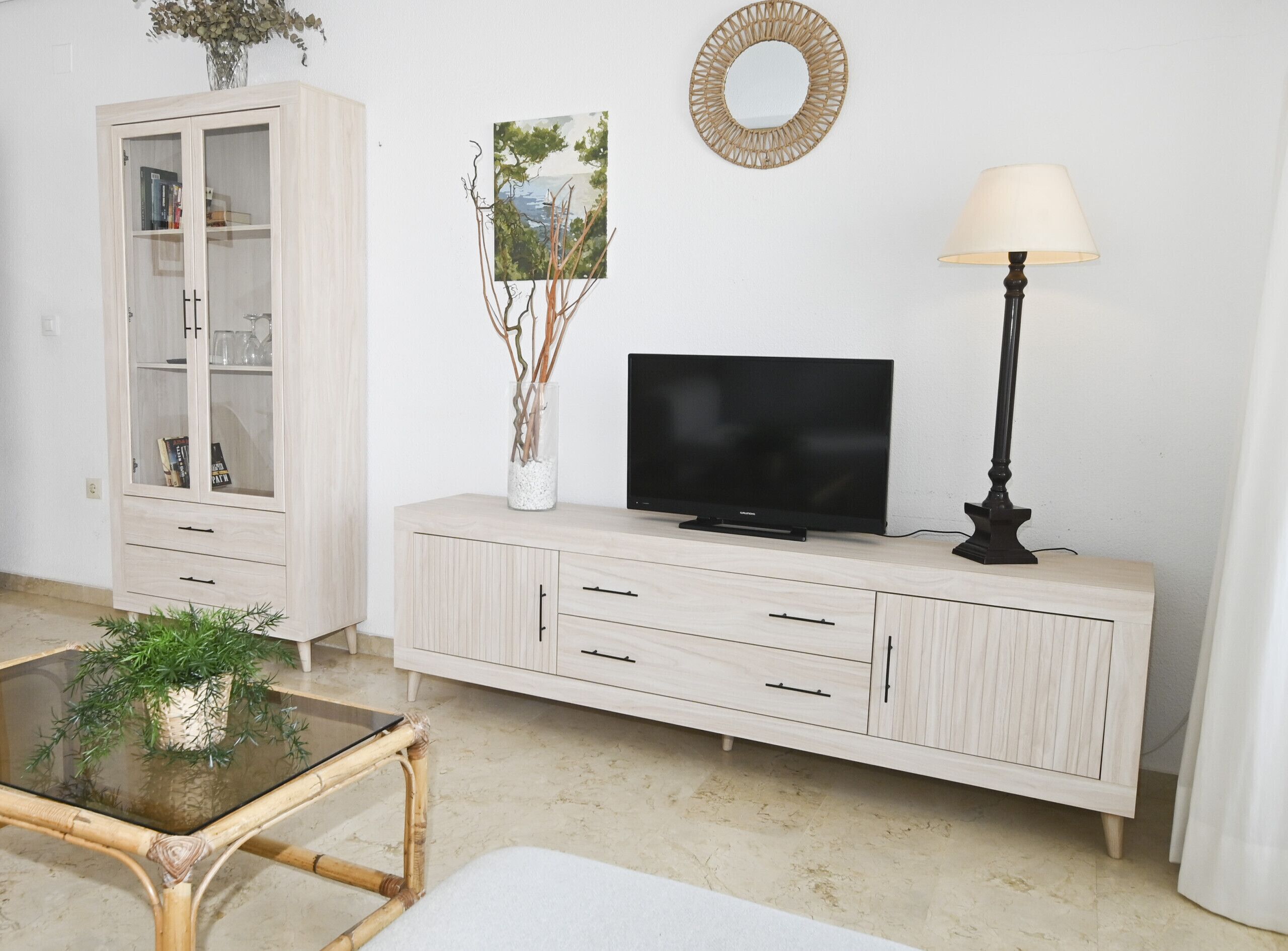 Un salon comprenant un téléviseur, un meuble, une lampe et une table en verre sur laquelle est posée une plante.