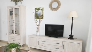 Een woonkamer met een televisie, een kast, een lamp en een glazen tafel met een plant.