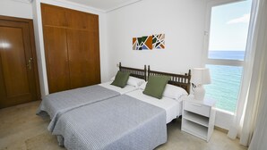 Een slaapkamer met twee bedden, een kledingkast, een nachtkastje met lamp en een raam met uitzicht op zee.