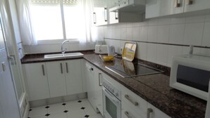 Een kleine keuken met witte kastjes, een magnetron, een fornuis en een spoelbak.