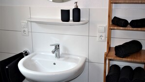 Un baño con un lavamanos blanco, un espejo y un estante con toallas negras.