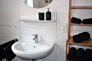 Une salle de bain avec un lavabo blanc, un miroir et une étagère sur laquelle sont posées des serviettes noires.