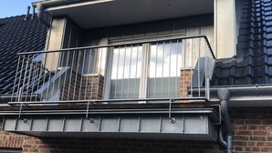 Ein Wohngebäude mit Backsteinfassade, einem Balkon mit Metallgeländern und einem Ziegeldach.