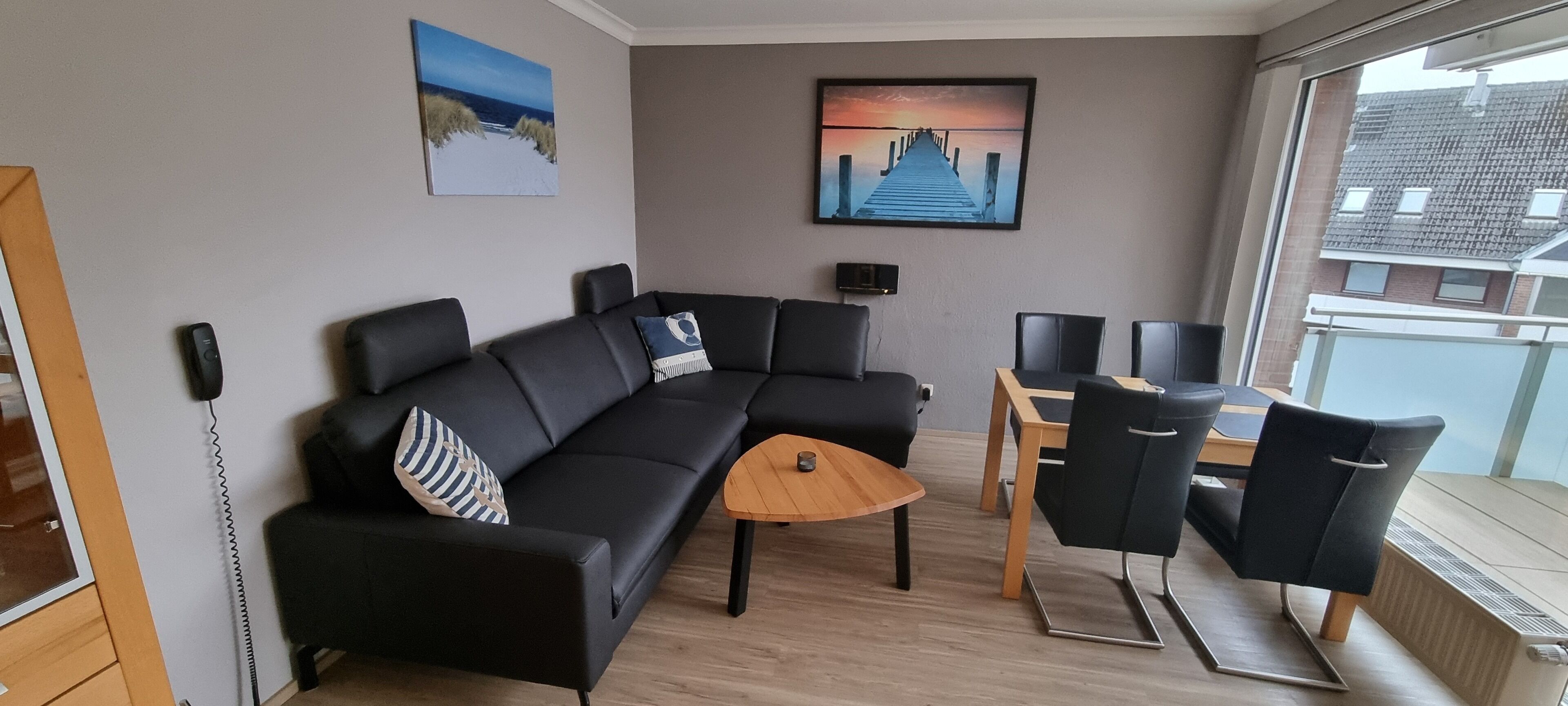 A modern living room with a black sectional sofa, a wooden coffee table, and a dining area with a table and chairs.