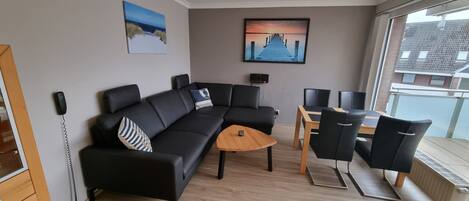 A modern living room with a black sectional sofa, a wooden coffee table, and a dining area with a table and chairs.