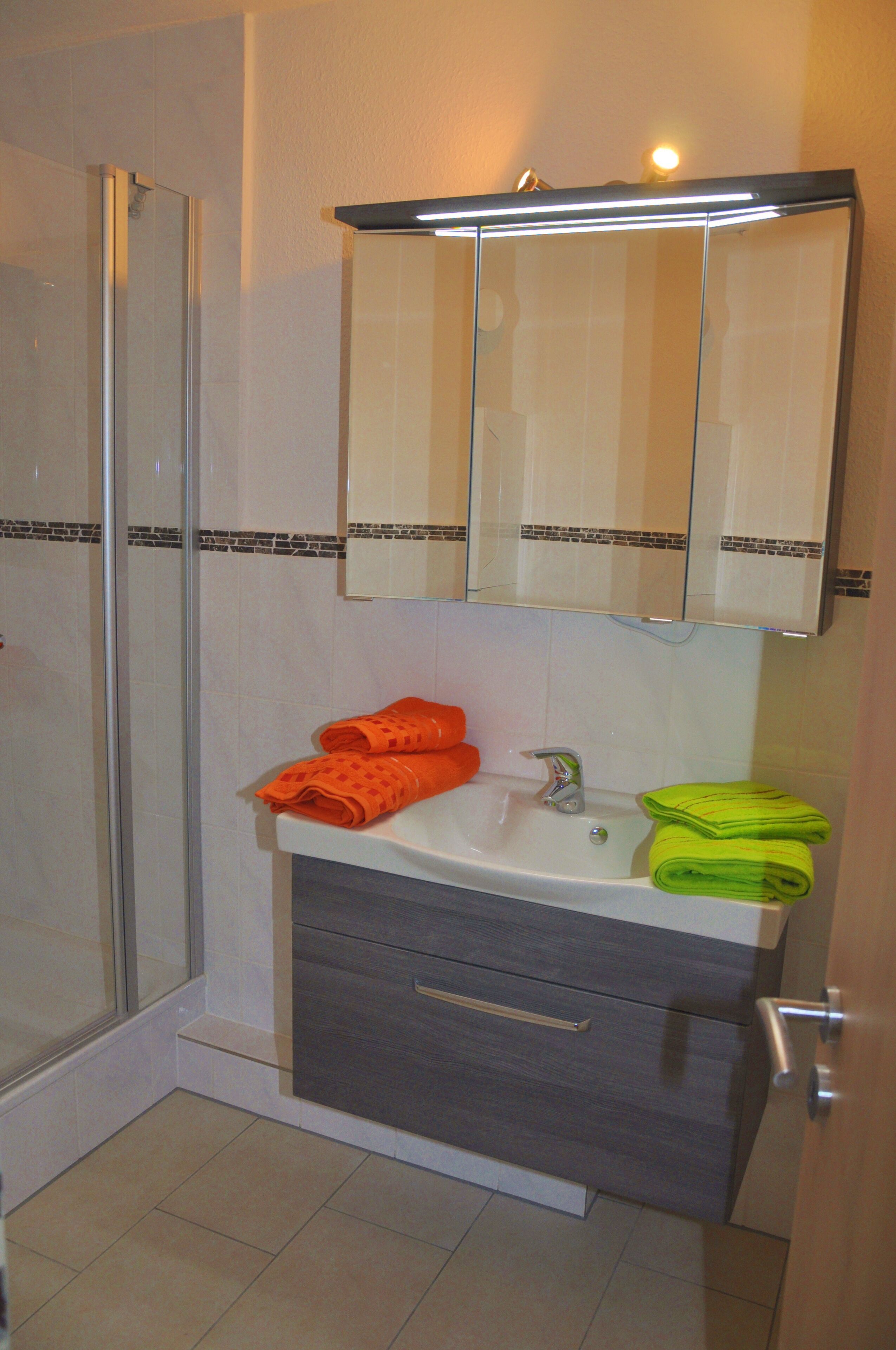 A bathroom with a glass shower enclosure, a sink with a mirror above, and two towels on the counter.