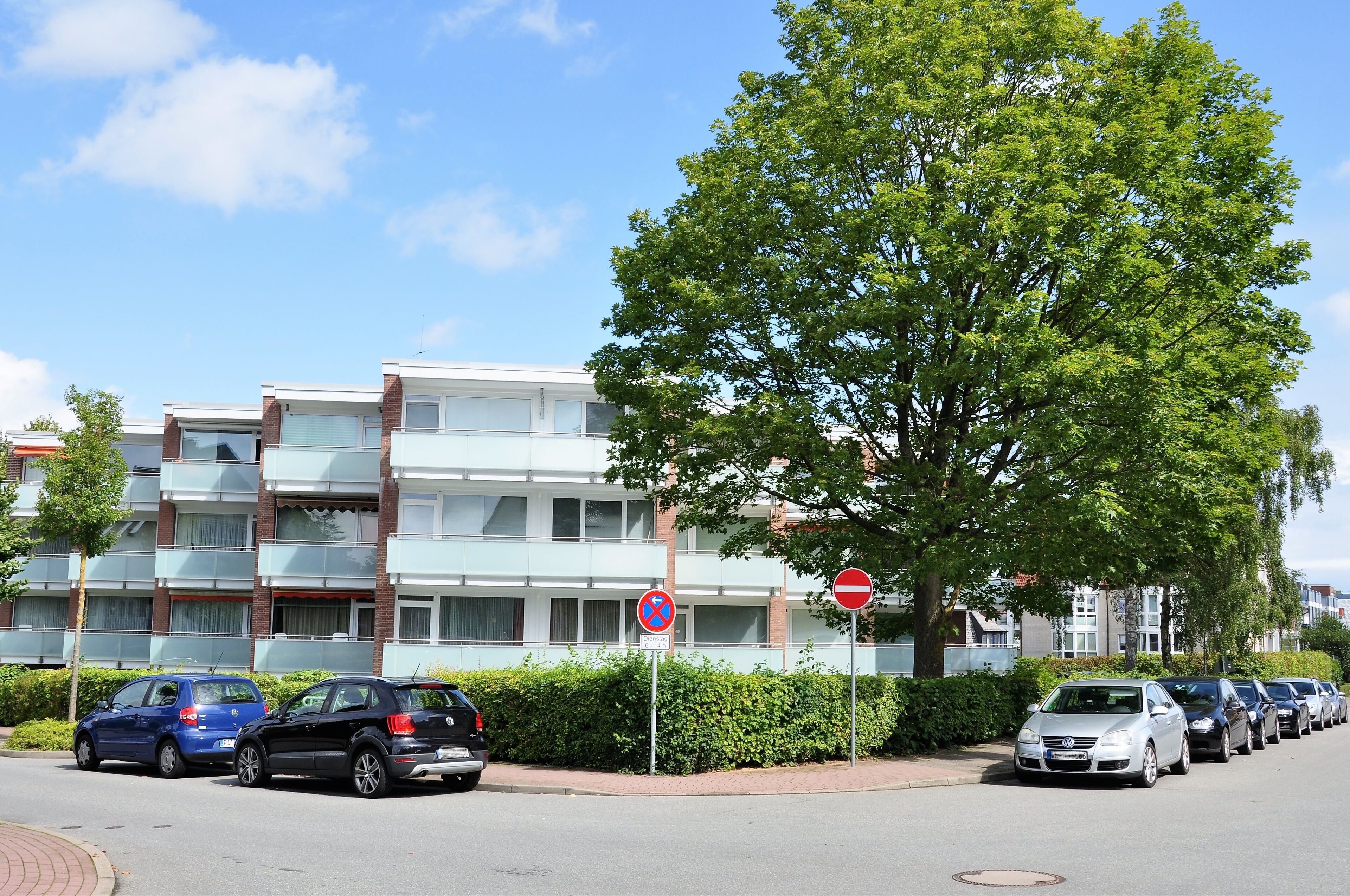 Une rangée de voitures garées le long d’une rue, avec un bâtiment en arrière-plan.