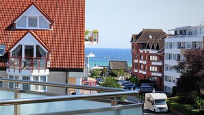 Una zona residencial costera con un edificio de tejas rojas, un balcón con barandilla roja y vistas al mar.