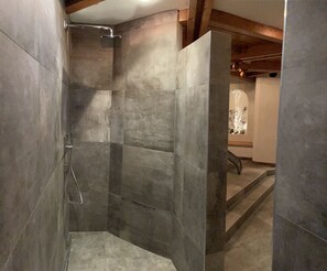 A shower area with tiled walls and a wooden ceiling beam.
