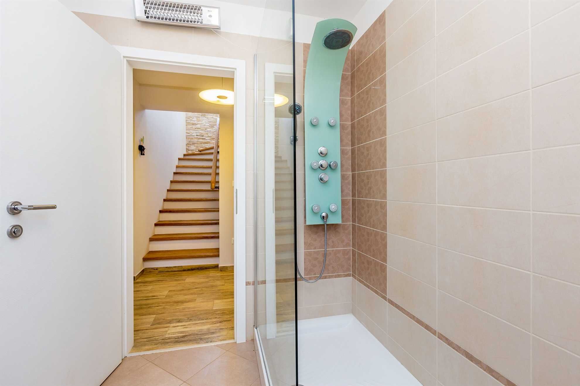 A shower with a glass door, a wooden staircase, and beige tiled walls.