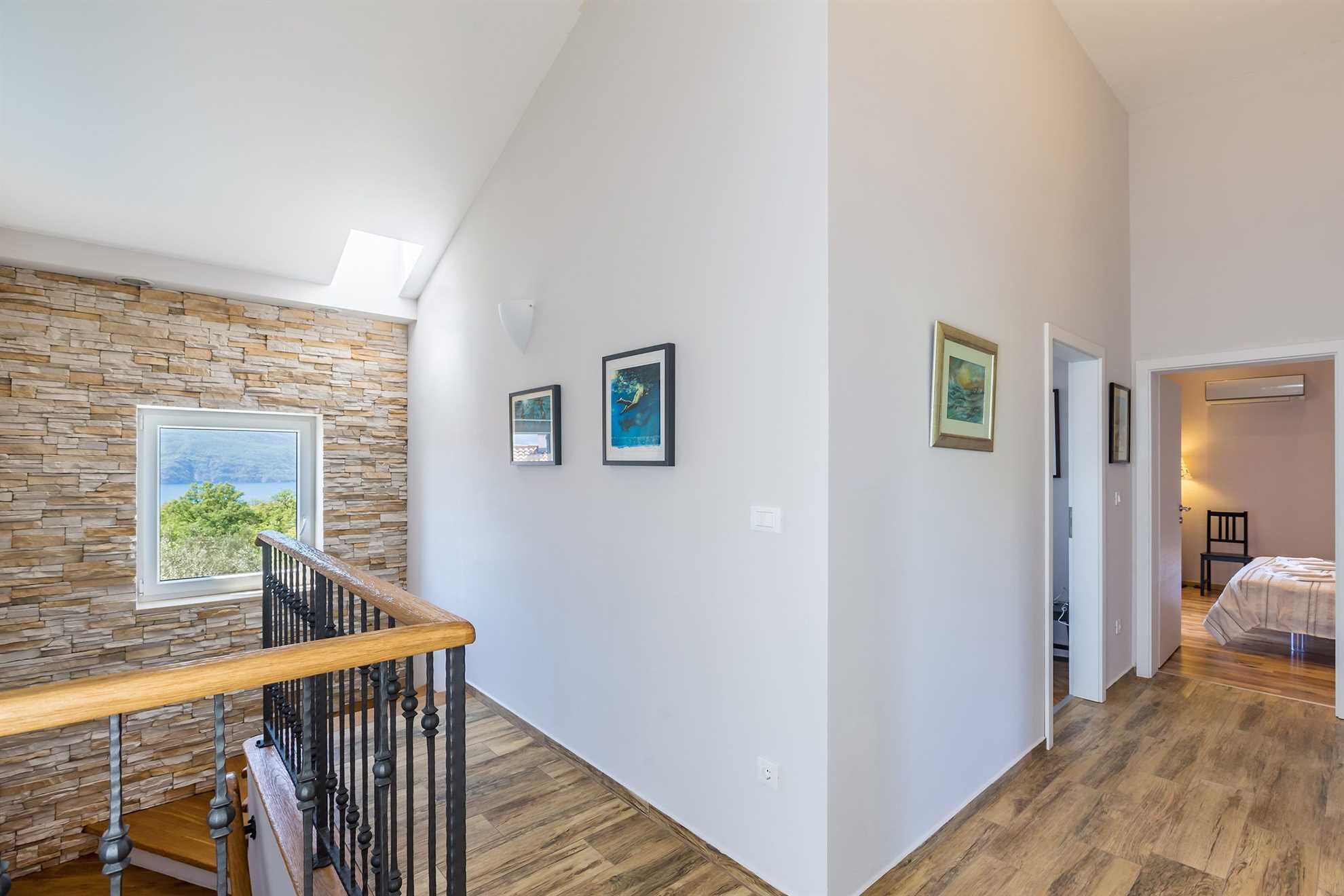 A spacious hallway with a stone wall, wooden flooring, and a staircase with a wooden handrail.