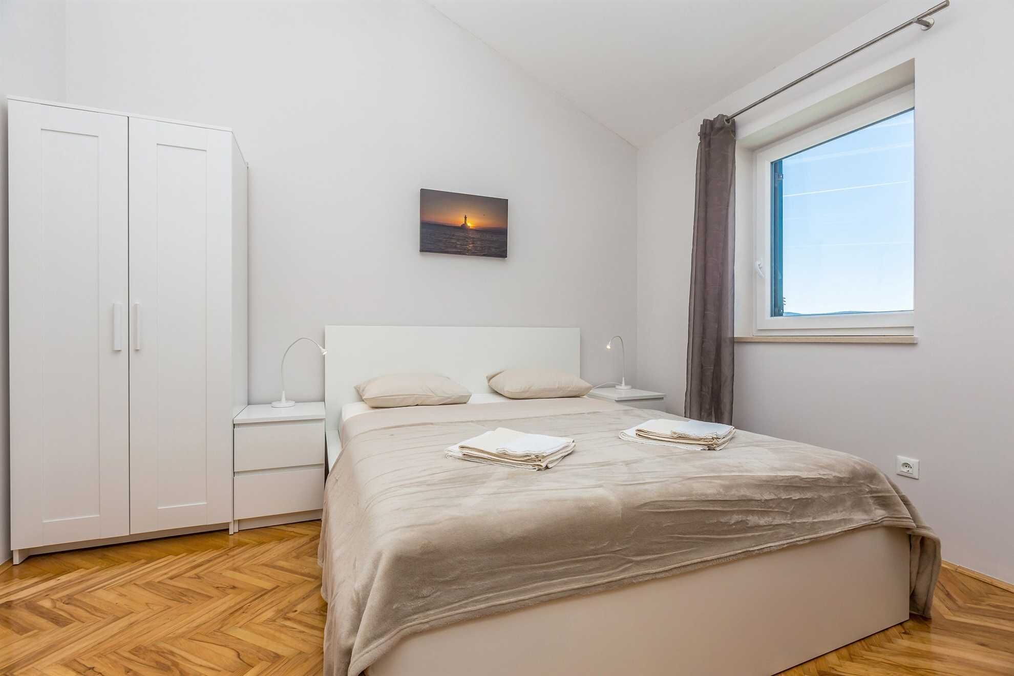 A bedroom with a bed, bedside tables, a wardrobe, a window with curtains, and a painting on the wall.