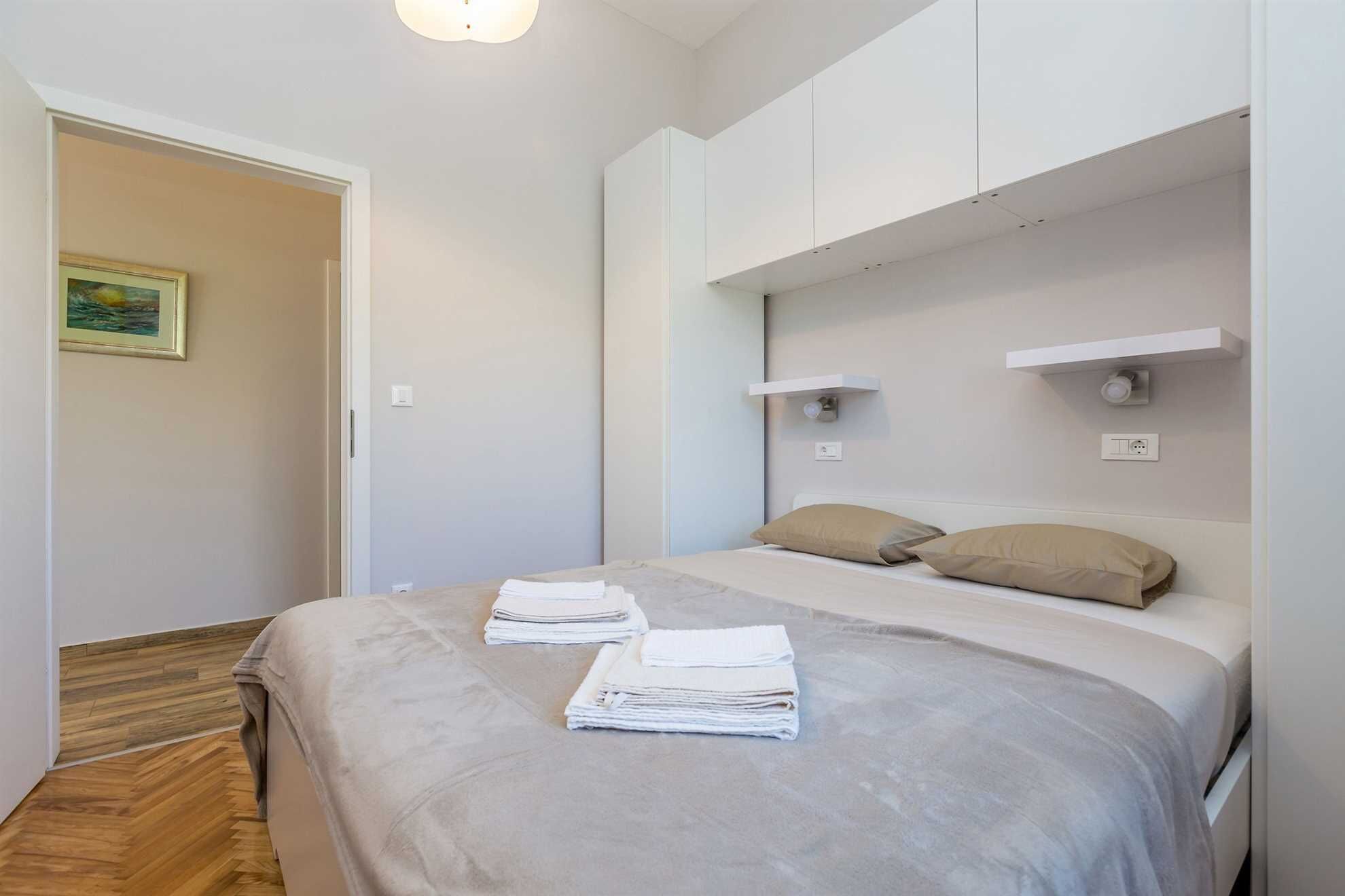 A bedroom with a bed, a nightstand, a wall-mounted shelf, and a painting on the wall.