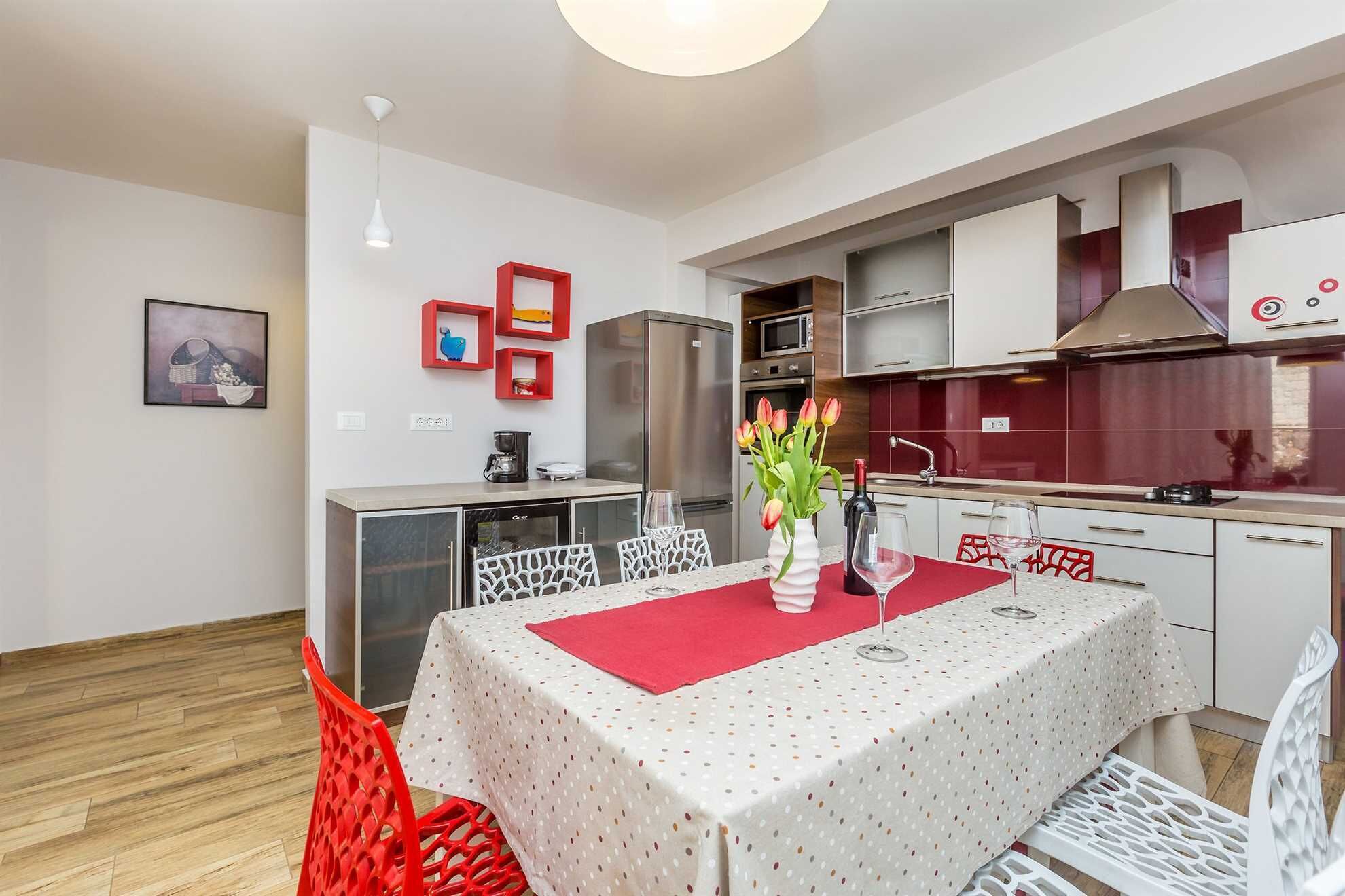 Una cocina moderna con armarios blancos, un refrigerador de acero inoxidable y un salpicadero rojo.