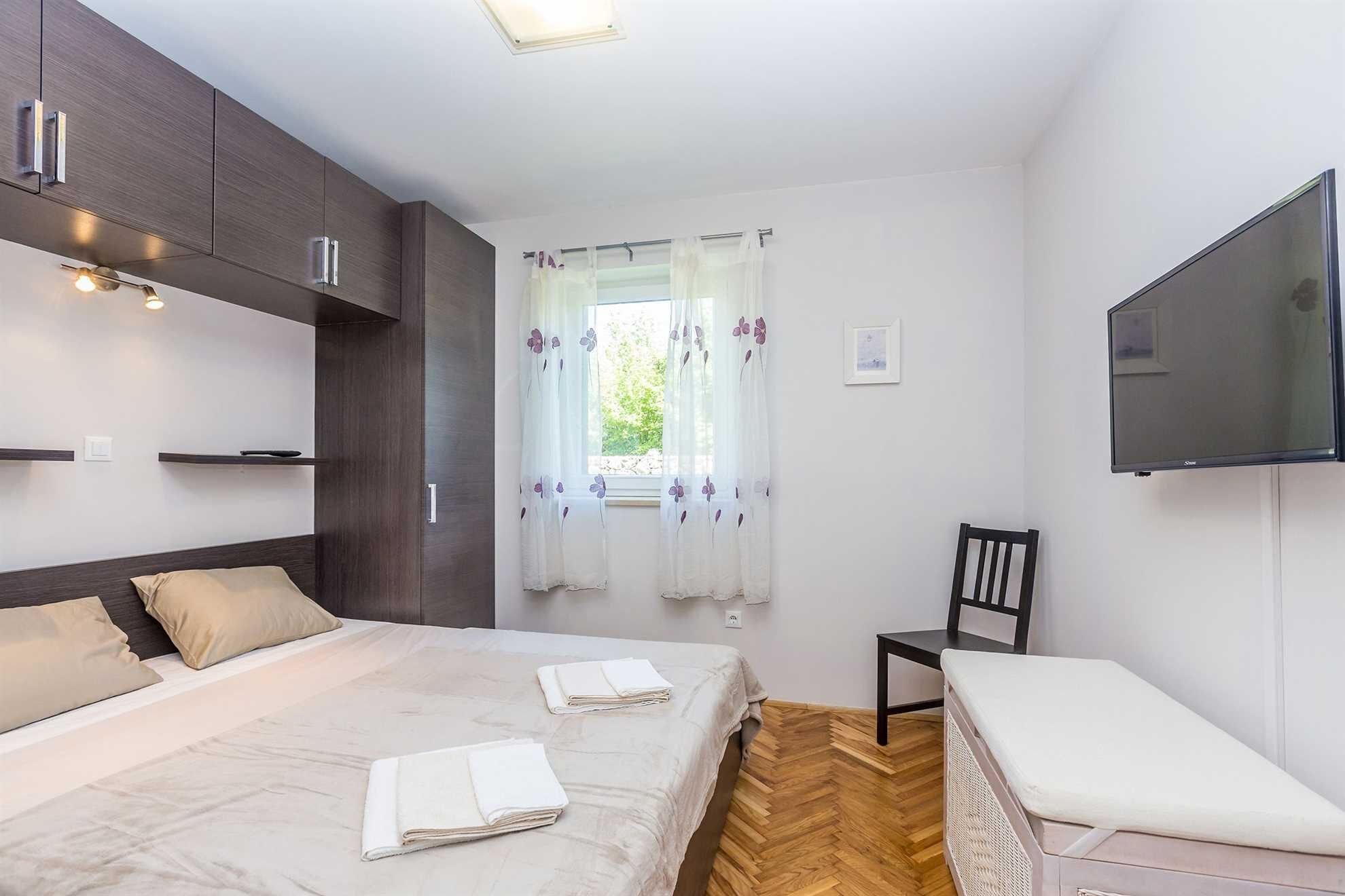 Een slaapkamer met een bed, nachtkastjes, een televisie en een raam met gordijnen.