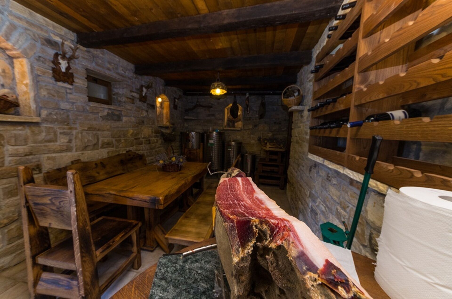 A rustic cellar with stone walls, wooden furniture, and a wine rack.