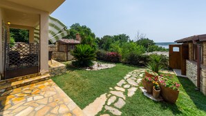 A well-maintained garden with stone pathways, a variety of plants, and a view of the sea.