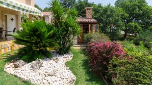 A small brick building with a tiled roof, surrounded by lush greenery and a stone pathway.