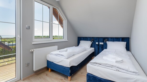 A bedroom with two single beds, a large window, and a view of the outdoors.