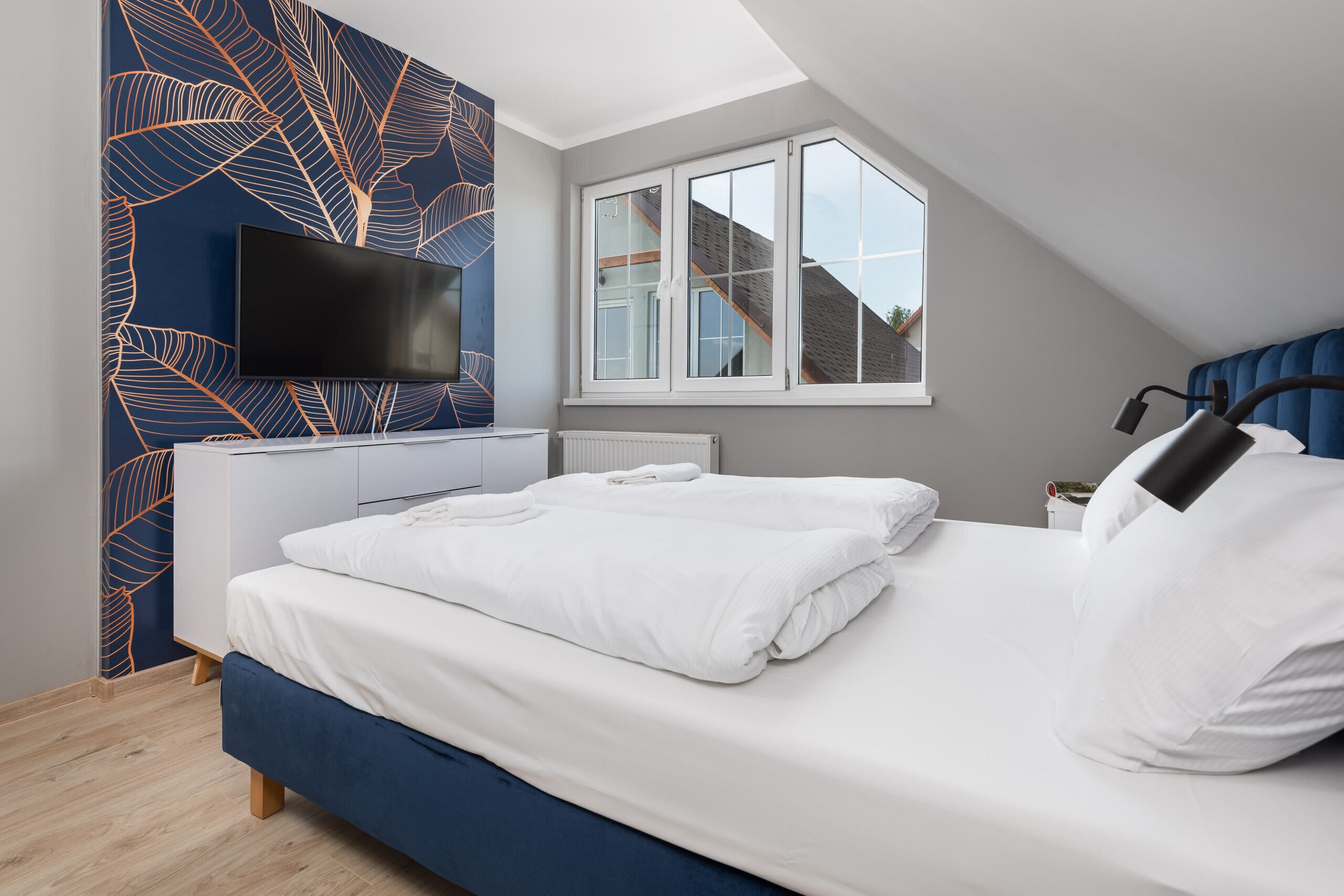 A cozy bedroom with a slanted ceiling, a neatly made double bed with crisp white linens, and a wardrobe in the corner, creating a welcoming atmosphere.