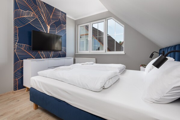 Une chambre à coucher avec un lit, un téléviseur fixé au mur, une fenêtre et un radiateur.