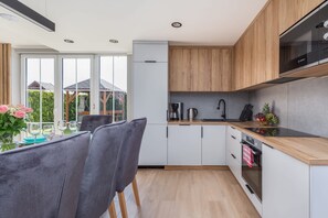 Eine moderne Küche mit Holzschränken, einem Bosch-Ofen und einem Essbereich mit grauen Stühlen sowie einem für zwei Personen gedecktem Tisch.