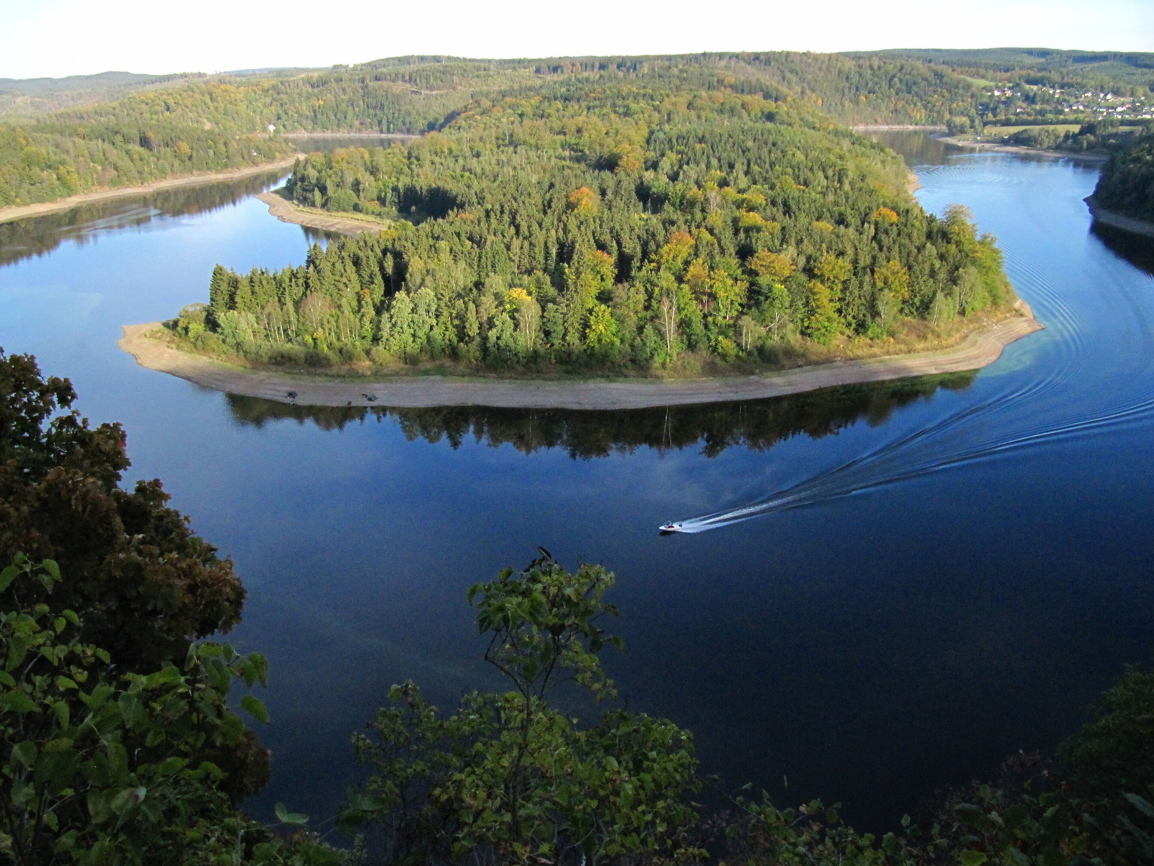 A lake surrounded by dense forest and a small island with a boat creating a wake.