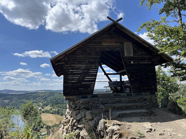 Una cabaña de madera con base de piedra, un cartel que indica su valor histórico y vistas del paisaje circundante.