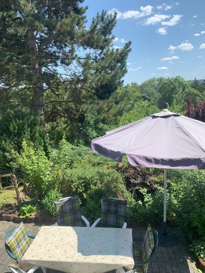 An outdoor patio with a table and chairs, surrounded by lush greenery and a large tree. - Directly at the Bleilochtalsperre - pure nature experience - Finnhütte Karli Saaldorf (Bad Lobenstein)