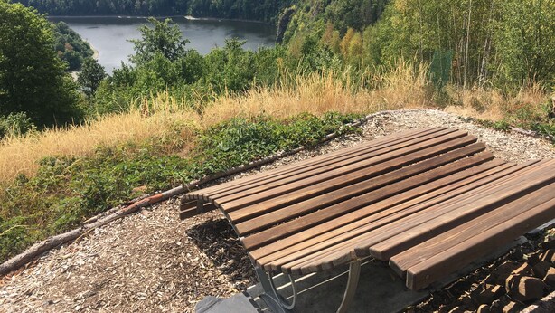 Un banco de madera con vista a un lago rodeado de colinas boscosas.