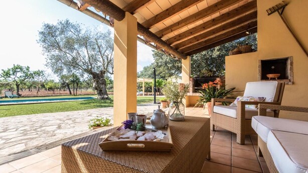 Un'area salotto esterna coperta con un tavolo in vimini, un divano bianco e una griglia per barbecue.