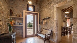 Un interno rustico con pareti in pietra, una panca in legno, un pavimento piastrellato e una porta che dà sull'esterno.