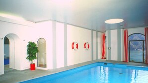 Una piscina interior con agua azul cristalina, paredes blancas y cortinas rojas.