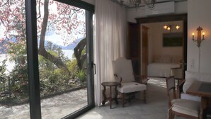 Una habitación con un amplio ventanal corredero que da a un jardín de cerezos en flor. En el interior, hay una mesa de madera con sillas, un sofá y una lámpara de araña.