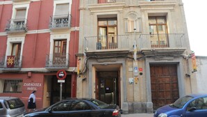 Un edificio de fachada roja, con un letrero que dice "Zaragoza Hostal" y una puerta de madera grande.