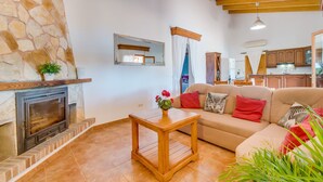 A cozy living room with a stone fireplace, a wooden coffee table, and a beige sofa with red cushions. - Rural finca with pool Can Grau Petit in Mallorca (Sencelles)