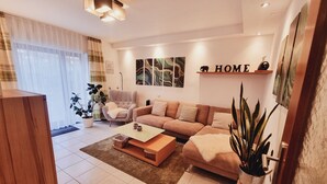 Ein modernes Wohnzimmer mit einer Couch, Sesseln, einem Couchtisch und einem großen Fenster mit durchsichtigen Vorhängen.