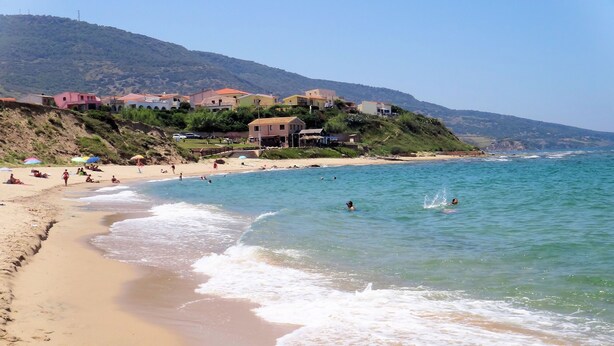 A beach with clear waters, people swimming, and houses on a hillside. - Holiday home on the sea in Sardinia - satellite TV, washing machine and sea view (Valledoria)