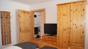 A bedroom with two beds, wooden wardrobes, a television on a dresser, and a door leading to another room. - Apartment avalanche stone (Bad Mitterndorf)
