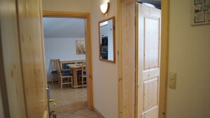 A narrow hallway with a wooden door, a mirror, and a dining area with a table and chairs. - Apartment avalanche stone (Bad Mitterndorf)