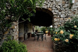 A stone archway leading to a patio with a table and chairs, surrounded by greenery and yellow roses.