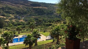 A terrace with a view of a swimming pool, lush greenery, and distant hills.