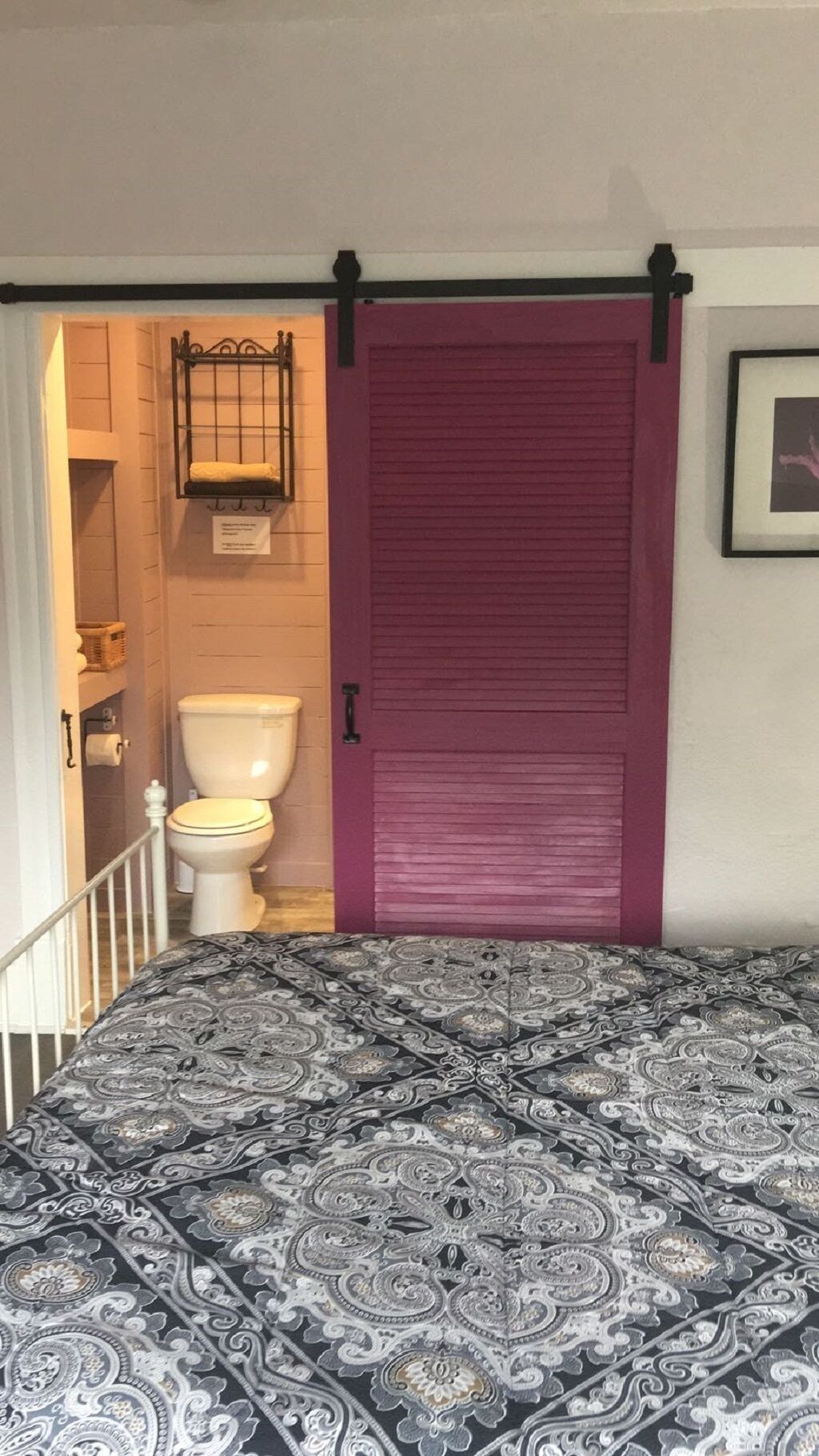 Une chambre avec un lit, une porte coulissante violette, des toilettes et une petite étagère sur laquelle se trouve un panier.