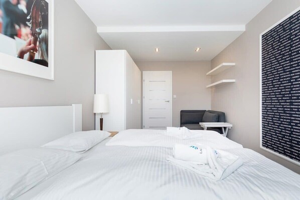 A modern hotel room with a neatly made bed, a desk with a chair, a lamp, and a wall with a list of city names.