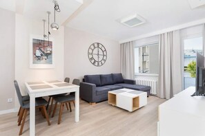 A modern living room with a dining table, sofa, and a large window with curtains.