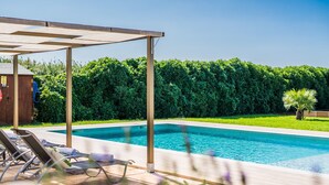 Une piscine entourée d’une végétation luxuriante, avec des chaises longues et une pergola.