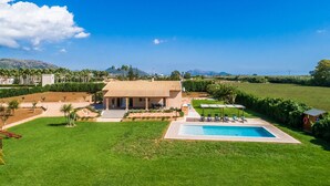 Une maison avec une piscine, entourée d’une pelouse bien entretenue et de palmiers.