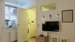 A room with a wooden floor, a white door, a radiator, a TV mounted on the wall, and a small wooden stool. - City Apartment in Frederiksberg with 2 bedrooms sleeps 4 (Frederiksberg)